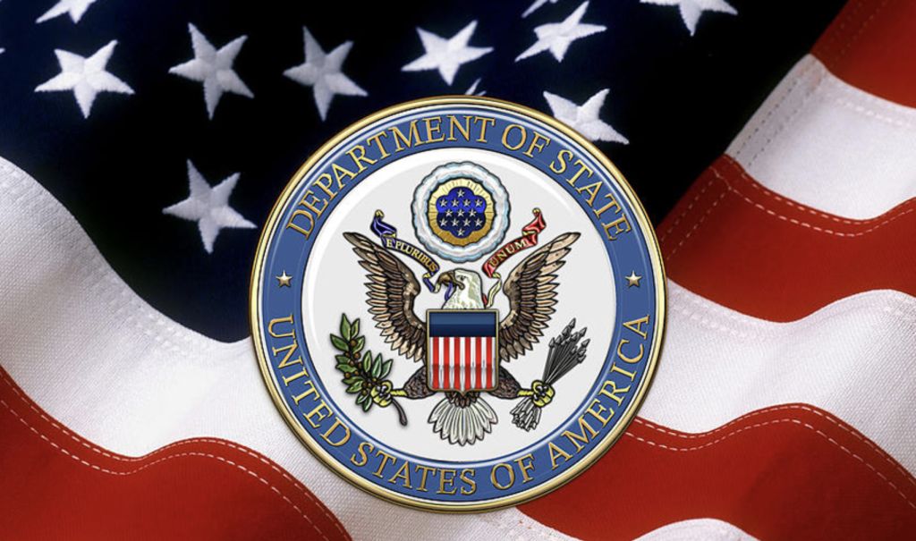 PER LA VERITÀ E PER IL DIRITTO. Sigillo del Dipartimento di Stato USA in evidenza. Sullo sfondo la bandiera degli Stati Uniti.