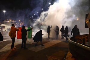 Manifestanti con la bandiera italiana affrontano la polizia all'ingresso del Porto Franco internazionale di Trieste.
